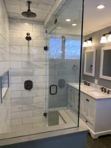 large shower door with grey and white tile in bathroom